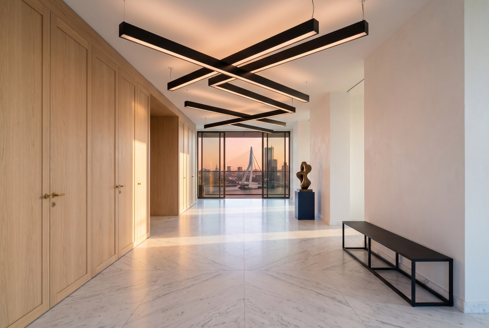 Entrance gallery with a white marble floor, oak joinery and crossing black steel light beams overhead