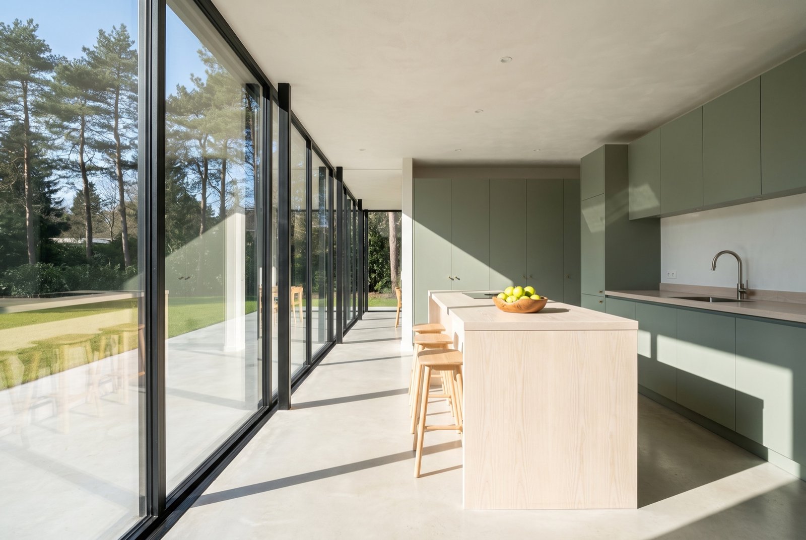 Kitchen in sage-green lacquer with an ash island top in front of a glass wall onto the garden
