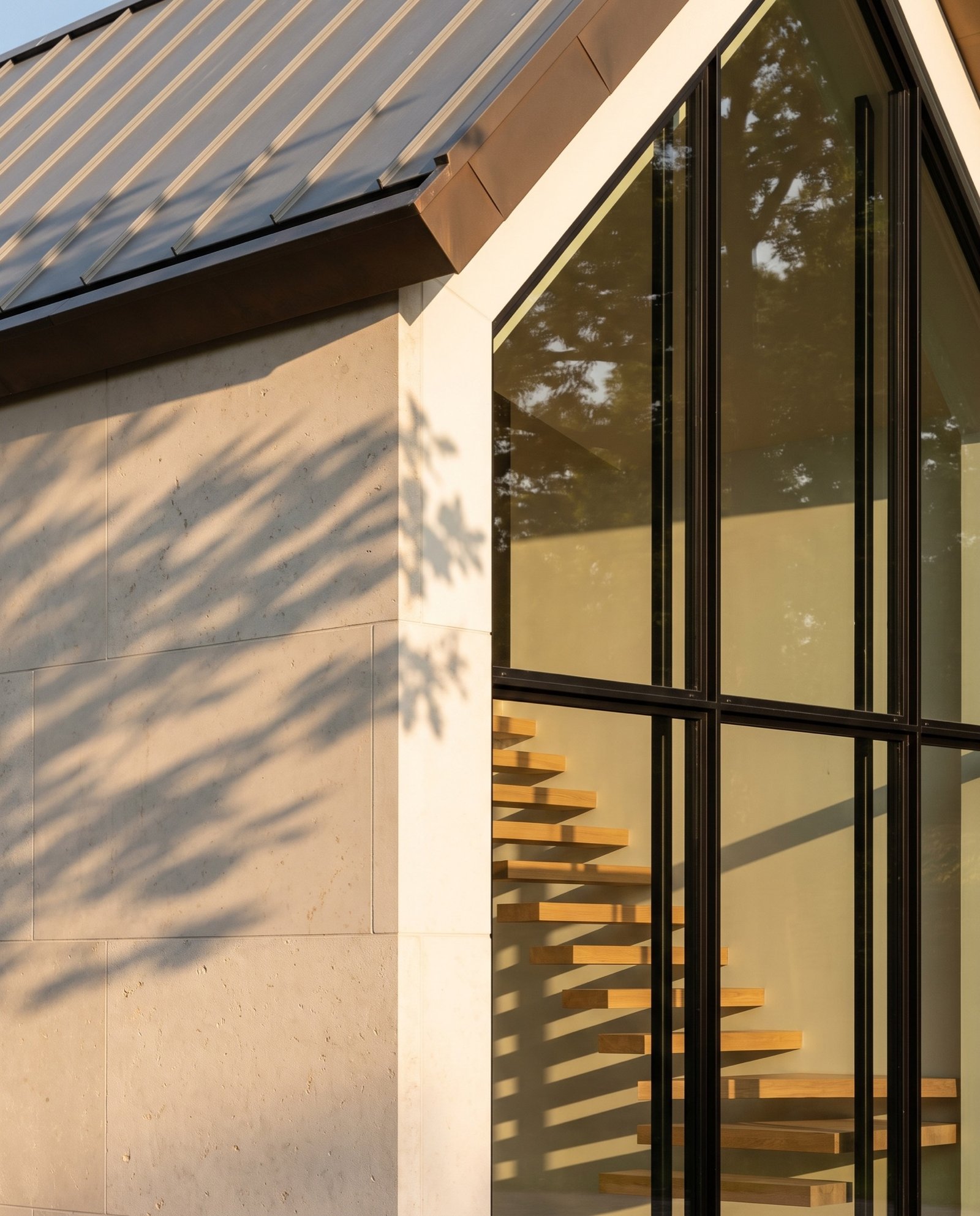 Corner where a limestone wall meets the glazed gable under a zinc roof edge